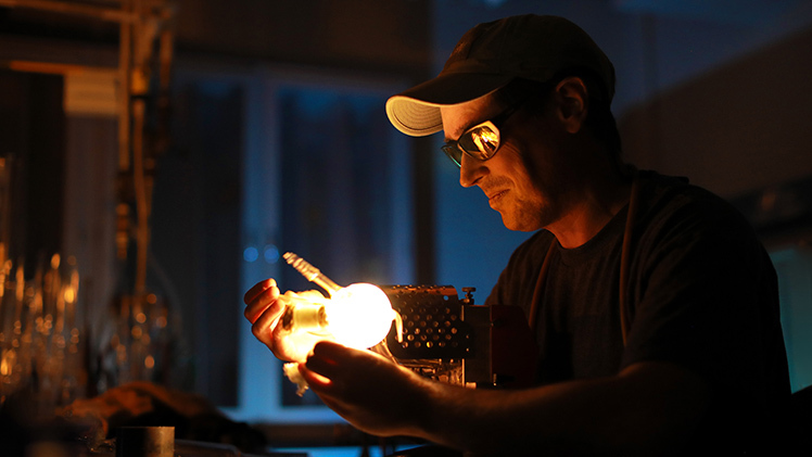 Eamon King, The University of Toledo’s scientific glassblower, works to make glass in his darkened lab.