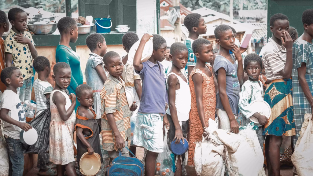 Bambini in attesa in una fila per la distribuzione di beni alimentari di prima necessità, un'immagine che riflette drammaticamente la portata delle crisi umanitarie e alimentari globali.