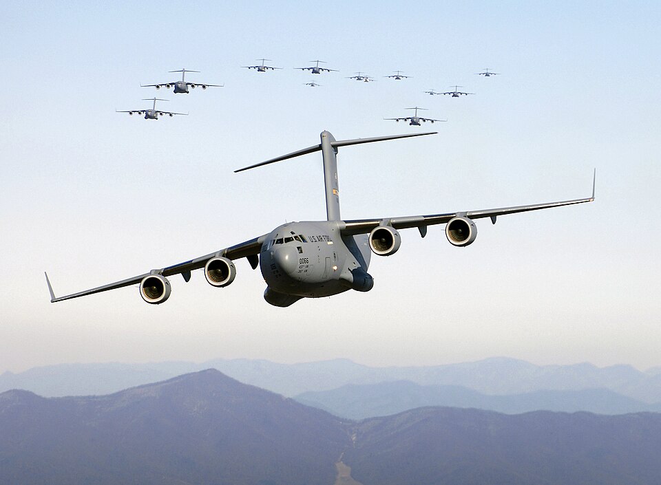 USA-Iran: tregua temporanea e bonifica degli esplosivi na formazione di aerei da trasporto militari C-17 Globemaster III in volo: la potenza aerea statunitense al centro del confronto e delle recenti tensioni con l'Iran.